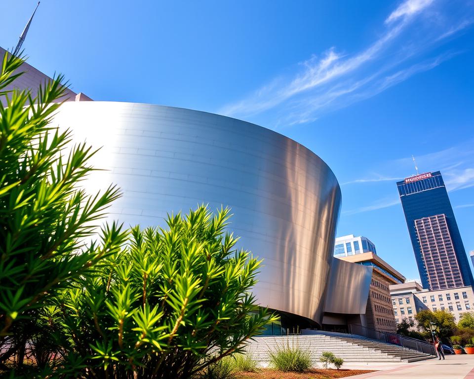 Walt Disney Concert Hall in Downtown Los Angeles, showcasing its iconic stainless steel exterior, reflecting sunlight with a dazzling shimmer. In the foreground, lush greenery and small garden elements frame the building, enhancing the urban landscape. The middle ground focuses on the sweeping curves and intricate architectural details of the concert hall, while the backdrop features a clear blue sky with a few wispy clouds, adding depth. The scene is bathed in warm, natural lighting, evoking a lively and inviting atmosphere. Capture the image from a low angle, emphasizing the grandeur of the structure against the skyline, ideal for highlighting Los Angeles's vibrant culture and artistic vibe. No people or distractions within the frame, just the concert hall and surrounding environment.